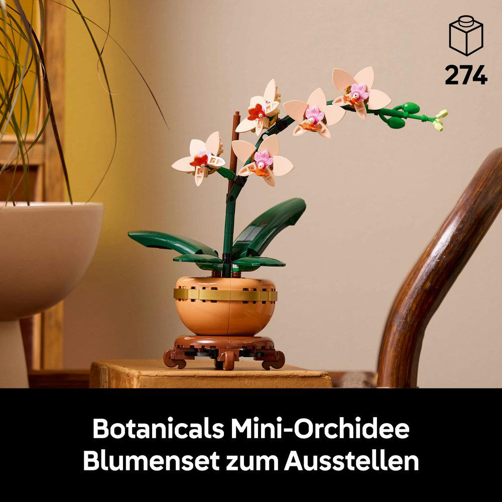 Lego Mini-Orchideenpflanze in einem Topf auf einem Holzständer. Beige Blüten mit pinkfarbenen Zentren und grünen Blättern.