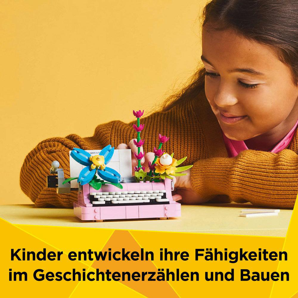 Ein Mädchen baut eine Lego-Schreibmaschine mit Blumen. Die Schreibmaschine ist rosa und blau. Ein Kind lächelt.