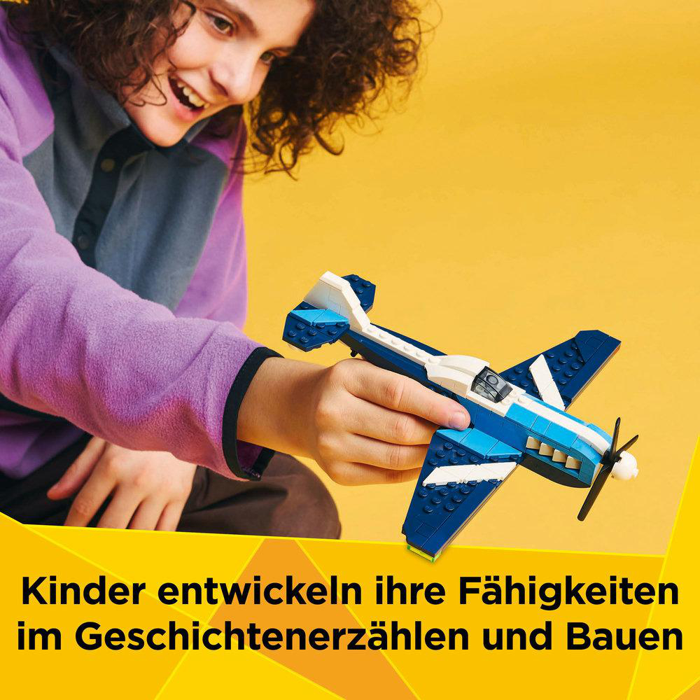 Kind spielt mit einem Lego-Flugzeug, blau und weiß, auf gelbem Hintergrund.