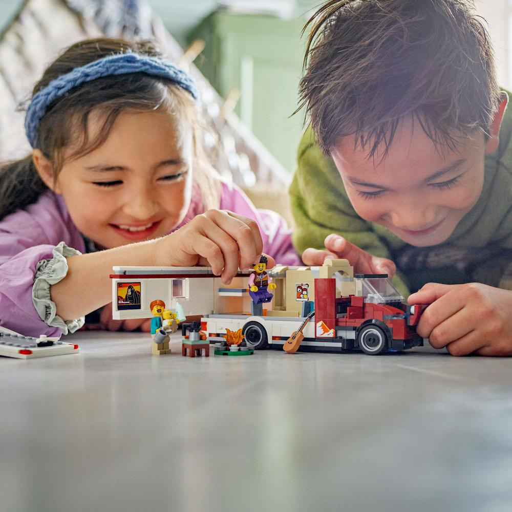 Zwei Kinder spielen mit einem Lego-Wohnmobil-Modell auf einer grauen Oberfläche.