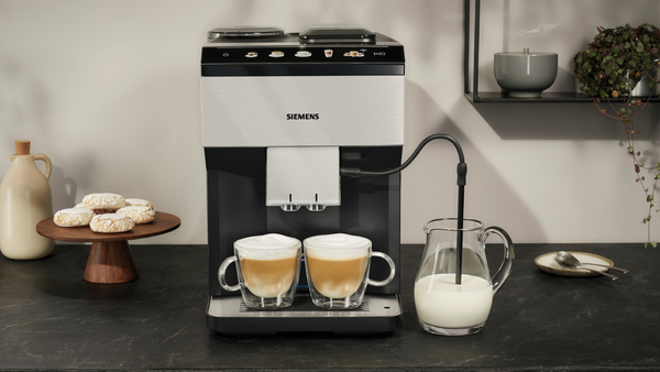 İki fincan, sütlük ve kurabiyelerle espresso makinesi. Koyu renk tezgah.