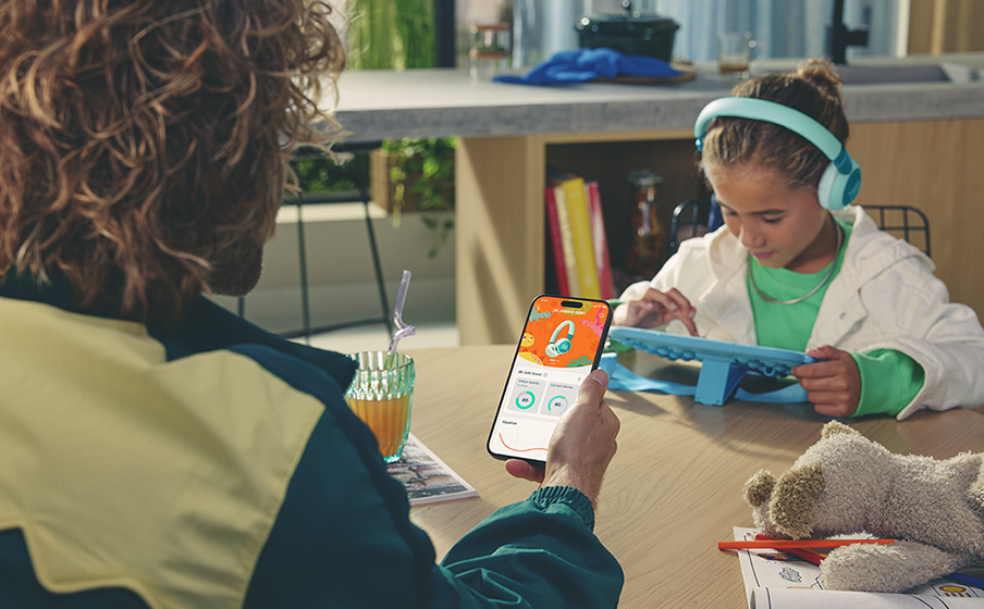 Bir adam, kulaklık uygulaması gösteren bir telefon tutuyor. Yakındaki bir kız, bir tabletin yanında kulaklık takıyor.