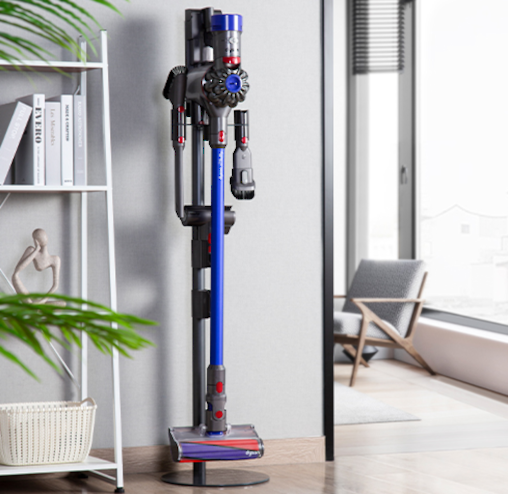 Odkurzacz z niebieskimi i czarnymi detalami na szarej ścianie. Biała półka i zielona roślina.