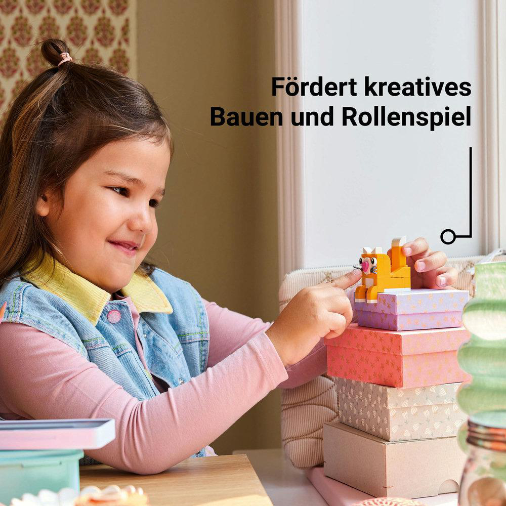 Ein Mädchen spielt mit Lego-Steinen und baut eine Katzenfigur auf bunten Boxen.