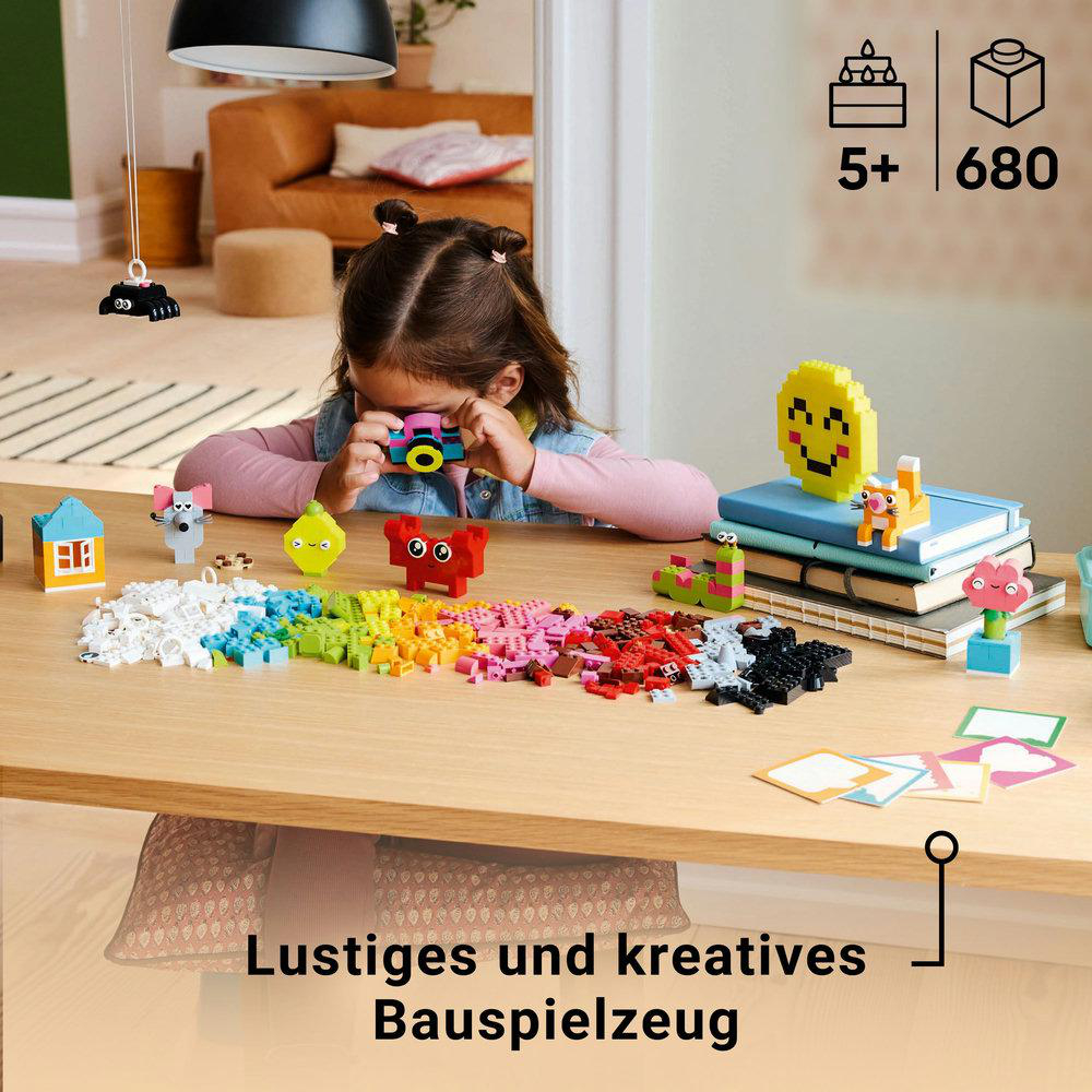 Ein Kind betrachtet eine Kamera, umgeben von Lego-Steinen und einem Tisch.