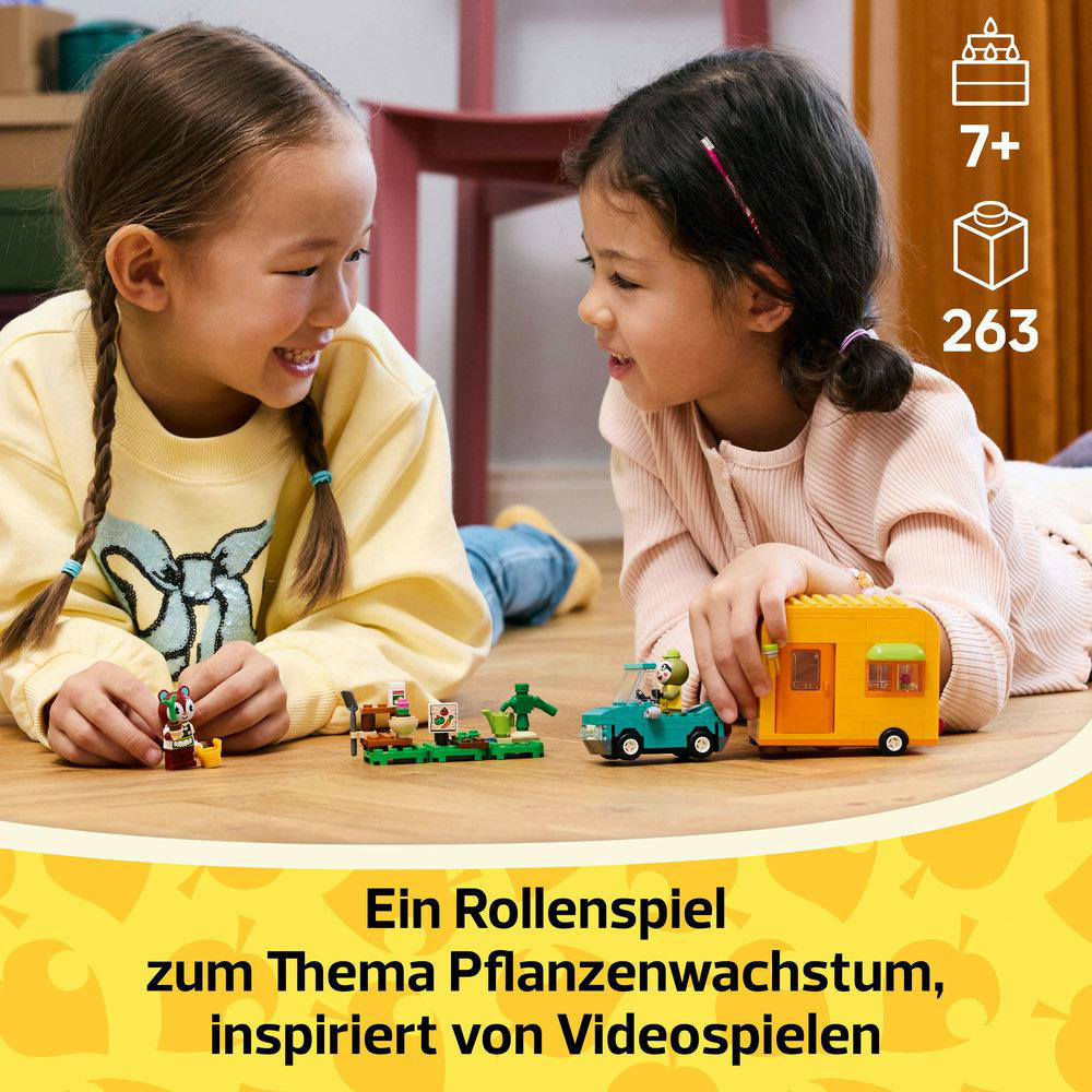 Zwei Mädchen lächeln, während sie ein Lego-Set betrachten. Ein Wohnwagen ist auf einer Holzoberfläche sichtbar.