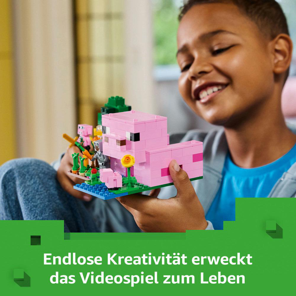 Kind spielt mit Lego-Set. Rosa Schweinehaus, Figuren und grüne Basis. Lächelndes Gesicht.