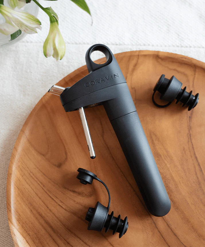 Ein Coravin-Wein-System und zwei Korken auf einem Holztablett. Das System ist schwarz und silber.