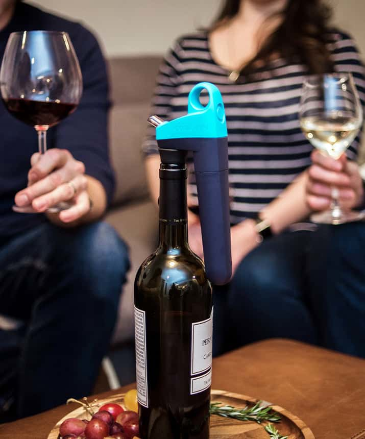 Eine Weinflasche mit einem Coravin-System, mit zwei Personen, die Weingläser halten.