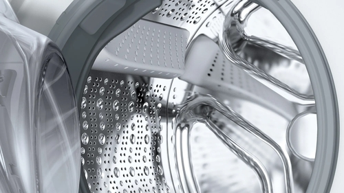 Primer plano del tambor de una lavadora. Interior metálico brillante con gotas de agua visibles.