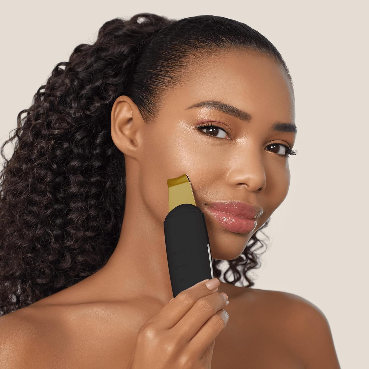 Mujer usando un dispositivo facial negro y dorado en su mejilla, frente a un fondo claro.