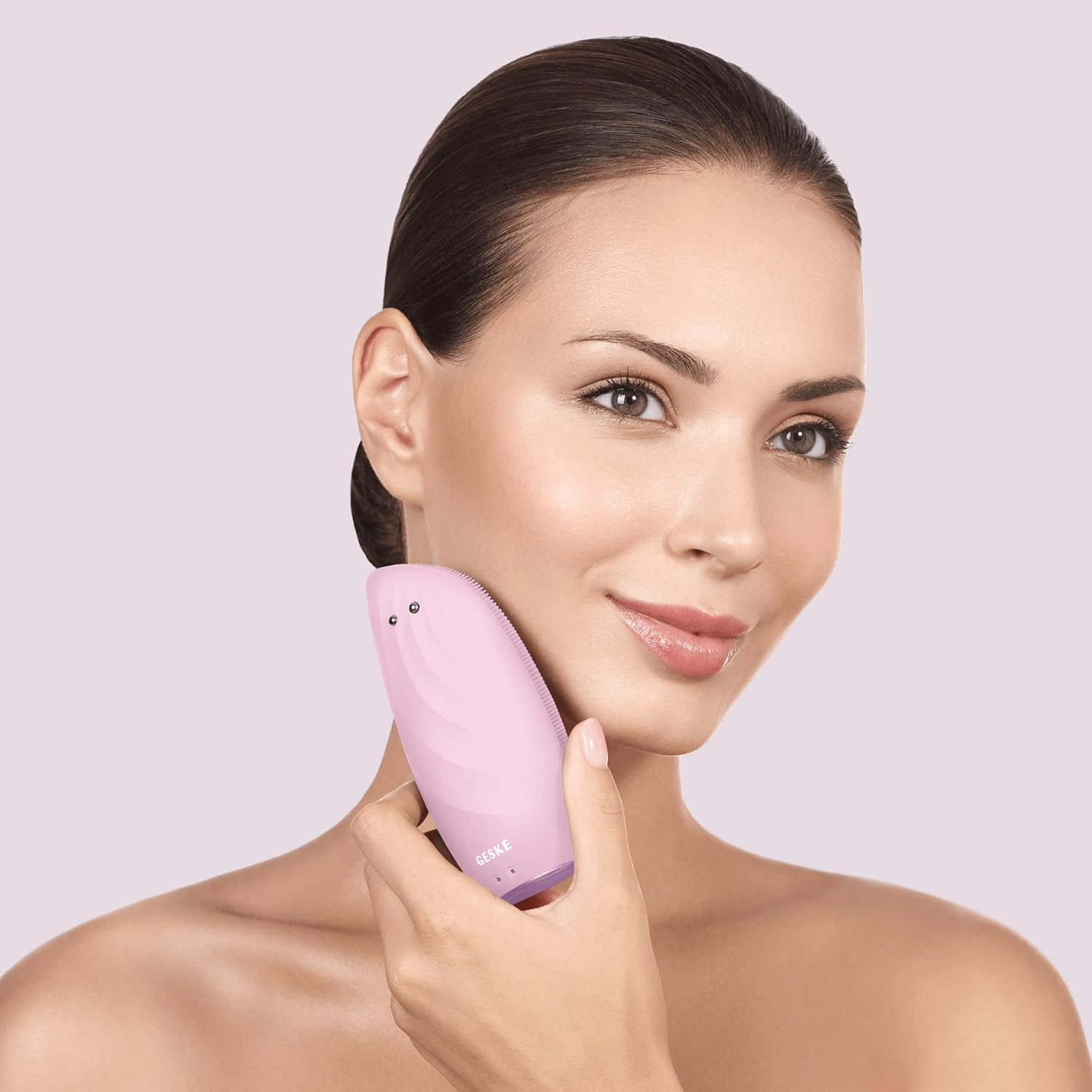 Una mujer con cabello oscuro usando un dispositivo de limpieza facial GESKE rosa en su rostro.