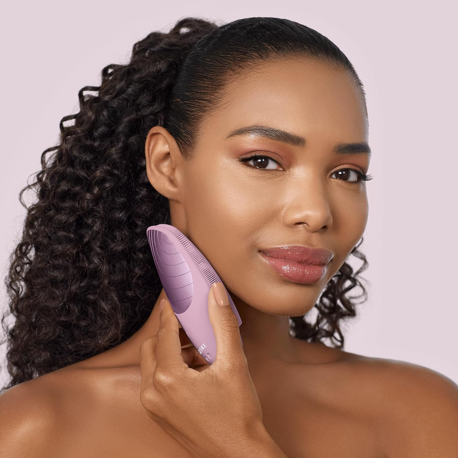 Mujer usando un cepillo de limpieza facial rosa en su rostro. Fondo rosa.