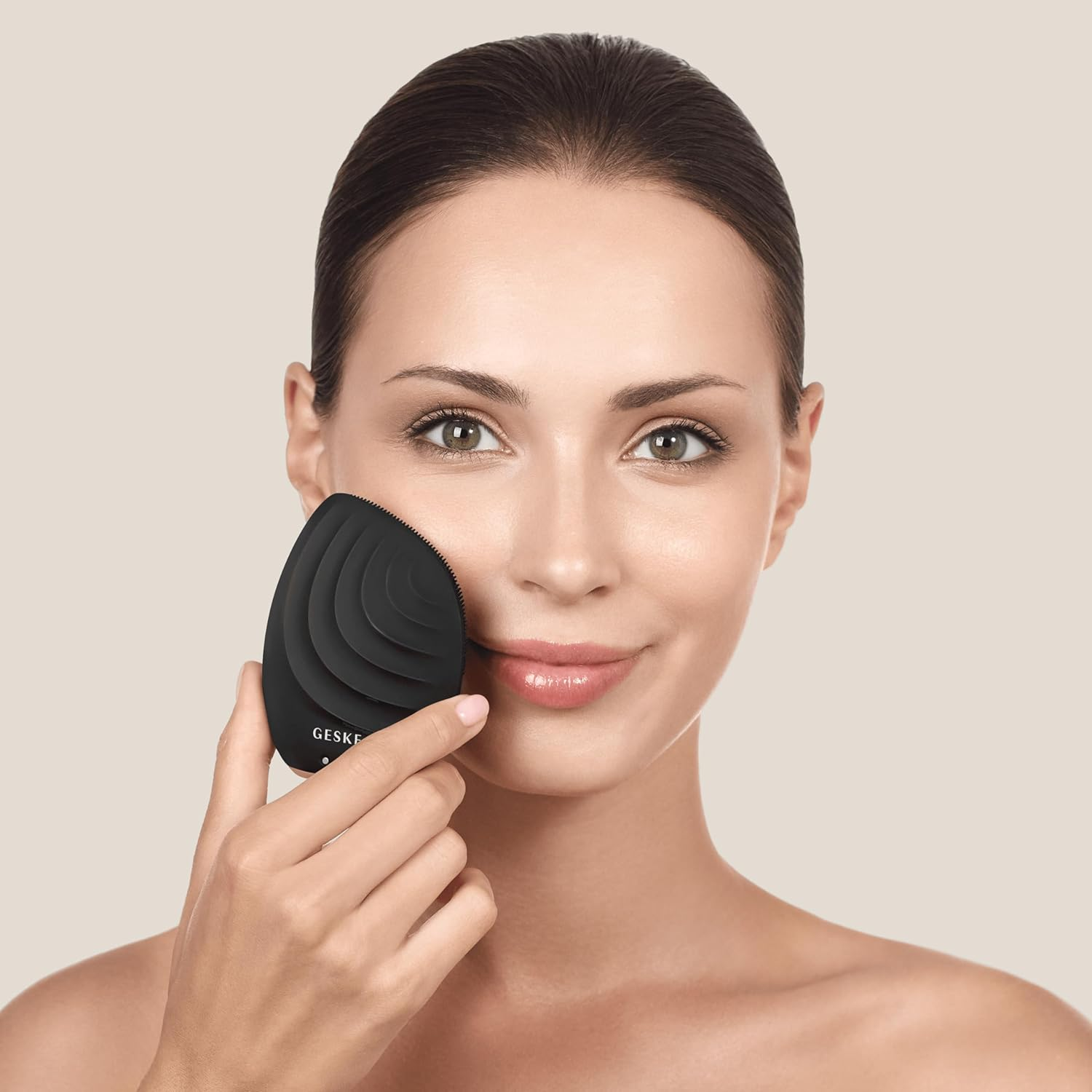 Mujer usando un limpiador facial Geske negro. Sonriendo, sosteniendo el dispositivo cerca de su mejilla.