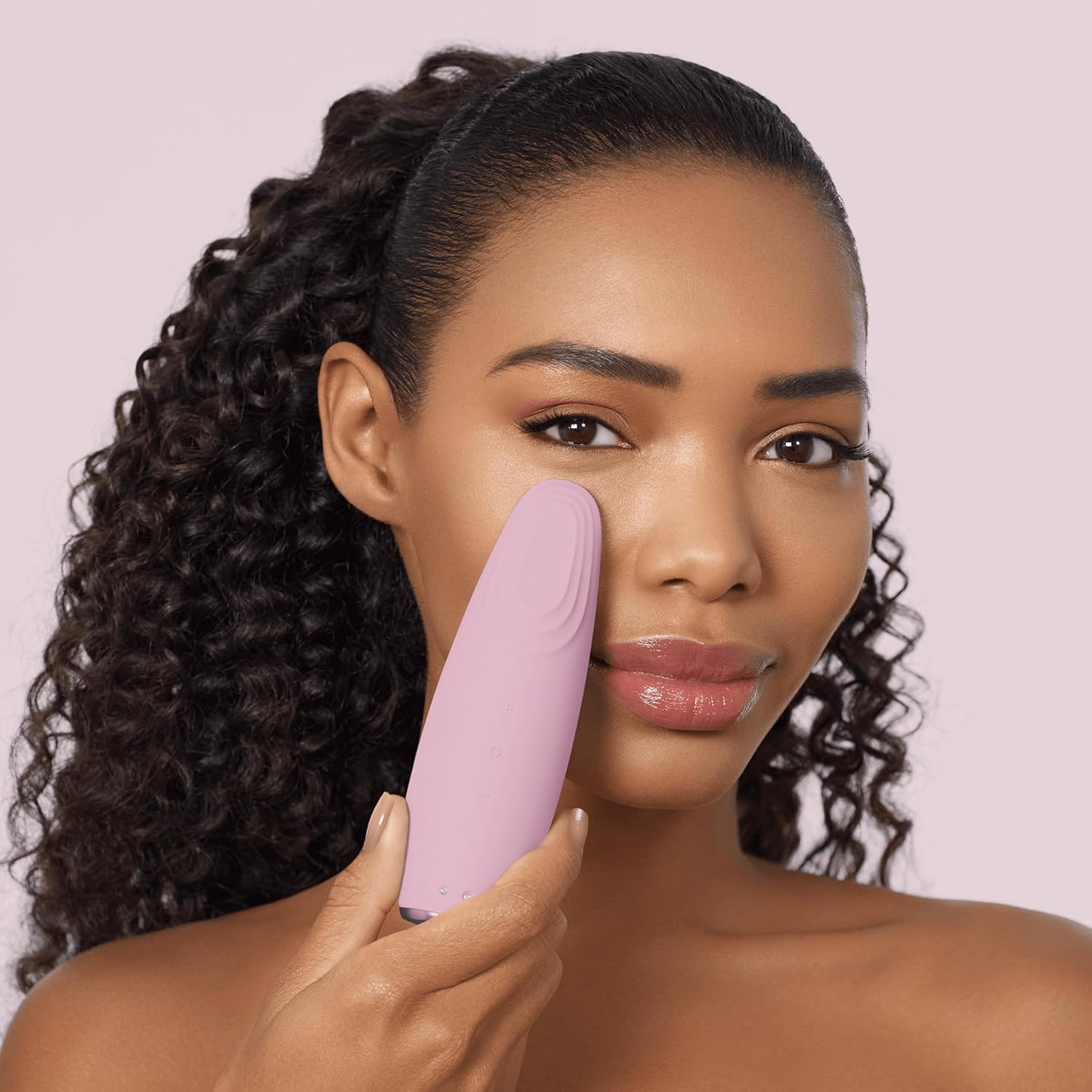 Mujer sosteniendo un dispositivo rosa de limpieza facial junto a su ojo.