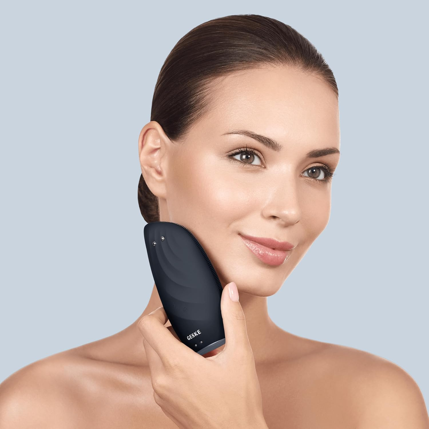 Una mujer usa un dispositivo facial negro en su mejilla. Sostiene el dispositivo.