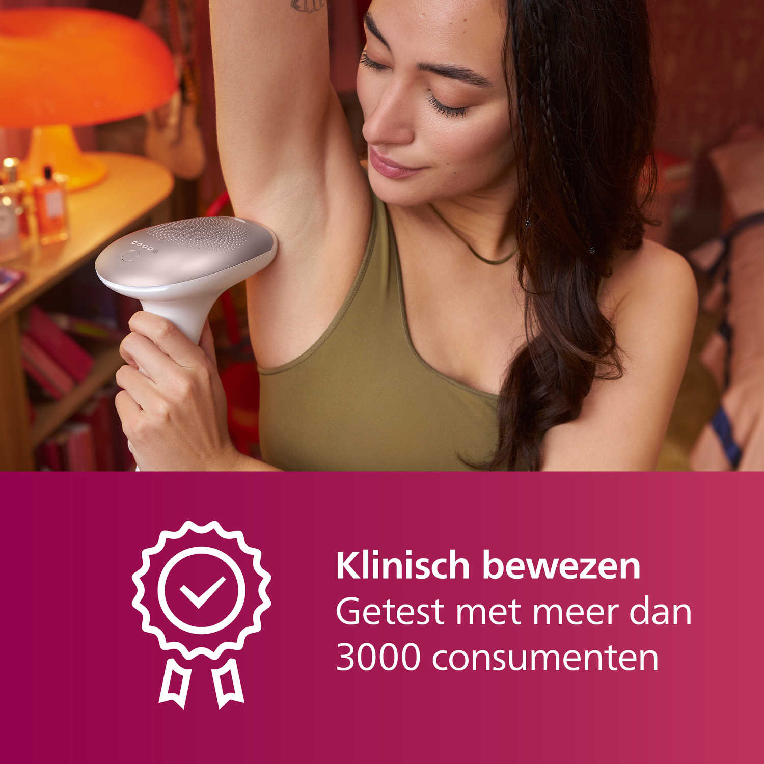 Een vrouw houdt een ontharingsapparaat onder haar arm. Ze draagt een groene top. De achtergrond is een kamer.