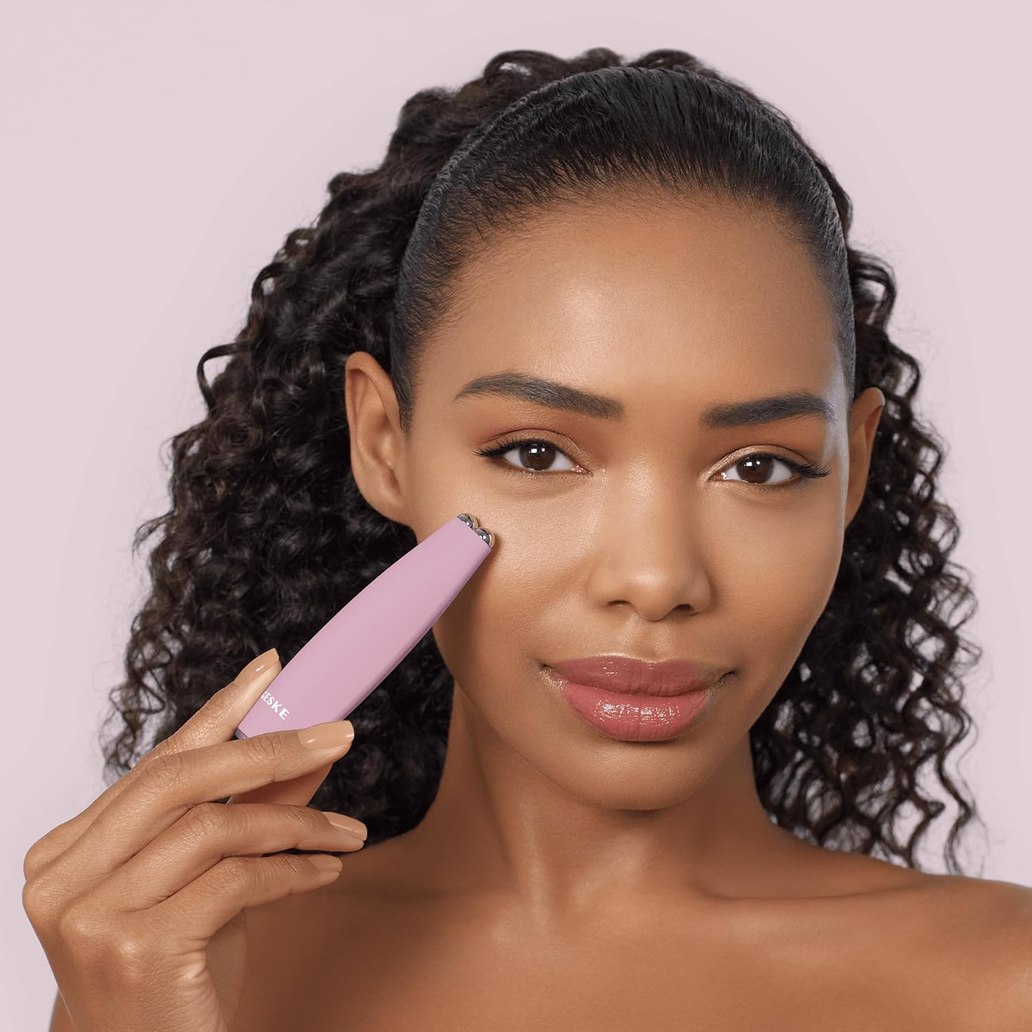 Mujer usando un dispositivo de belleza rosa en su rostro, mirando a la cámara.