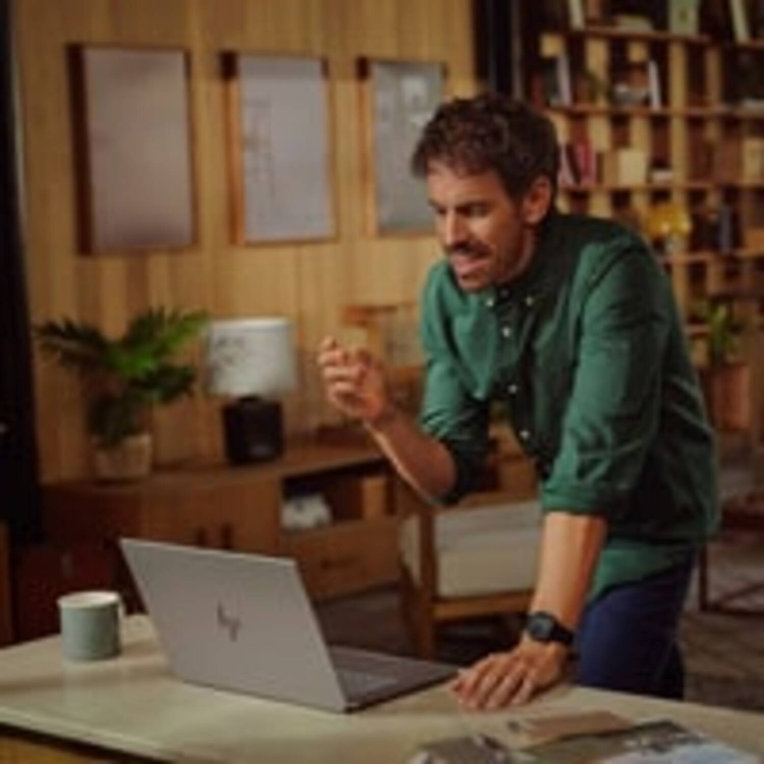 Man in green shirt gesturing while looking at a laptop on a desk.