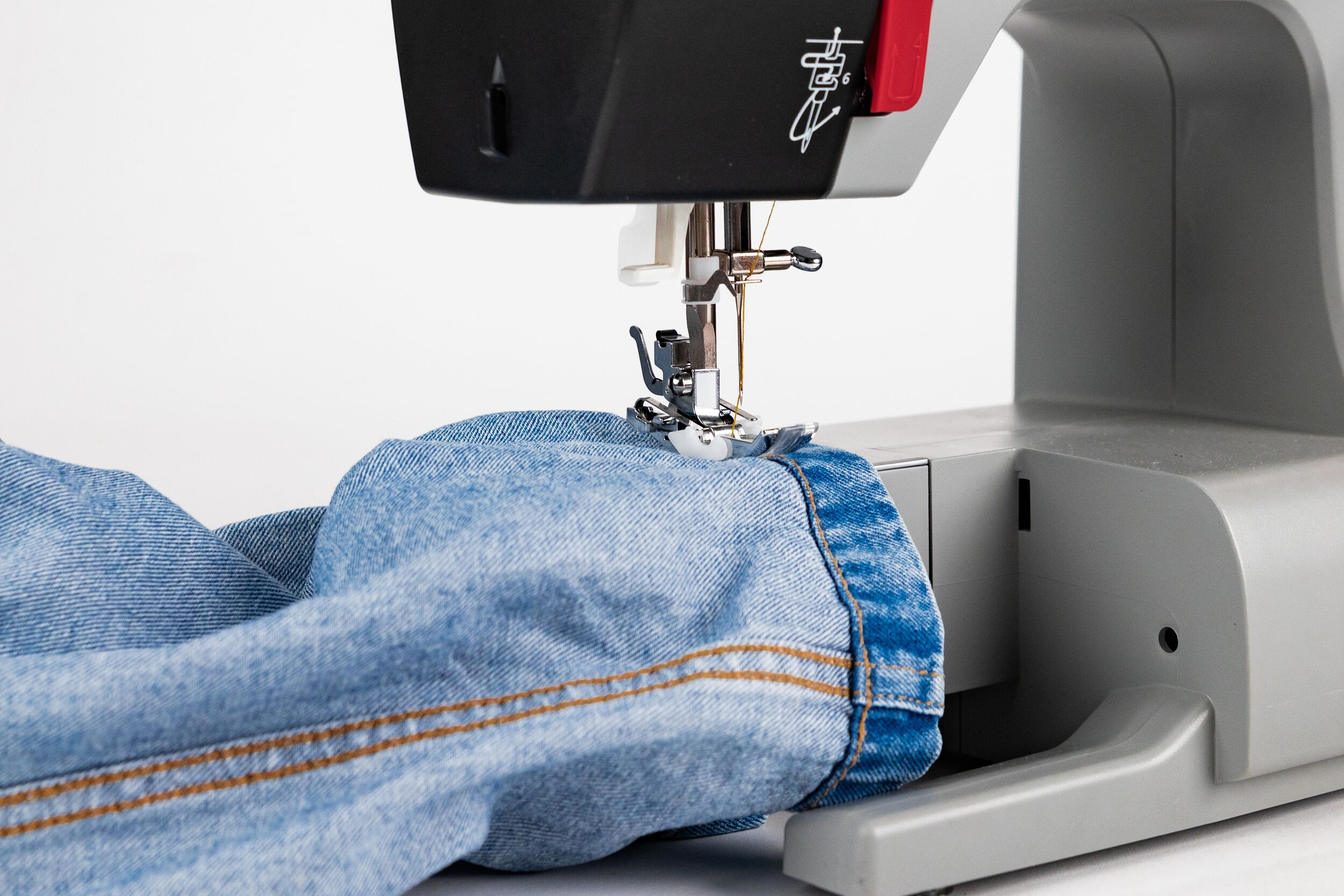 Eine Nähmaschine, die einen blauen Jeanssaum näht. Der Stoff ist rechts.