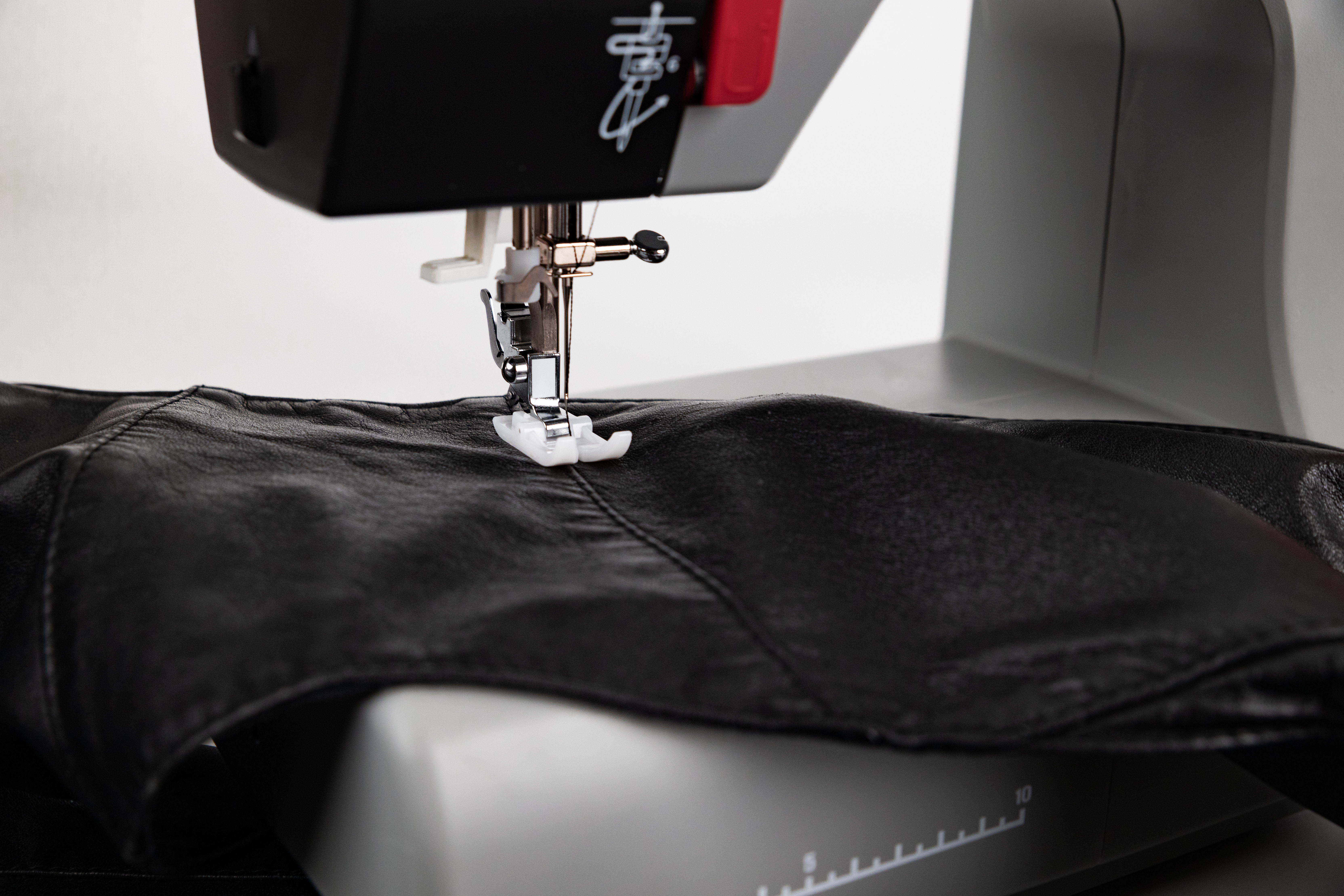 Eine Nähmaschine mit schwarzem Leder unter der Nadel. Die Maschine ist grau und rot.