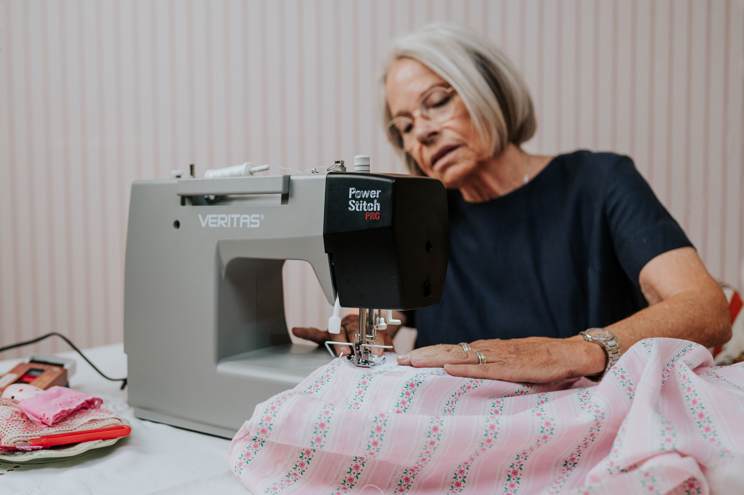 Eine ältere Frau näht rosa geblümten Stoff mit einer Nähmaschine.