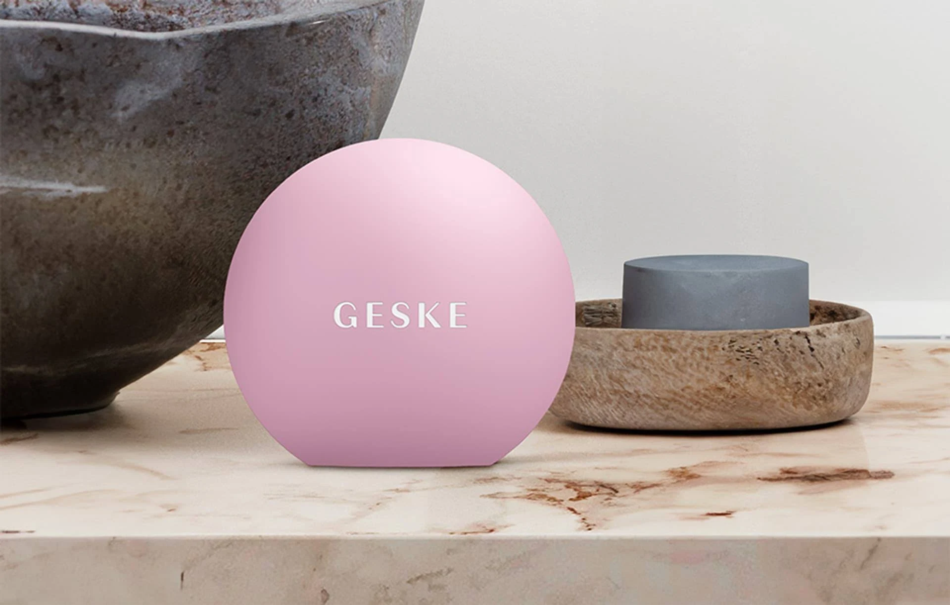 Masajeador facial GESKE rosa sobre mármol. Cuenco y jabón grises.