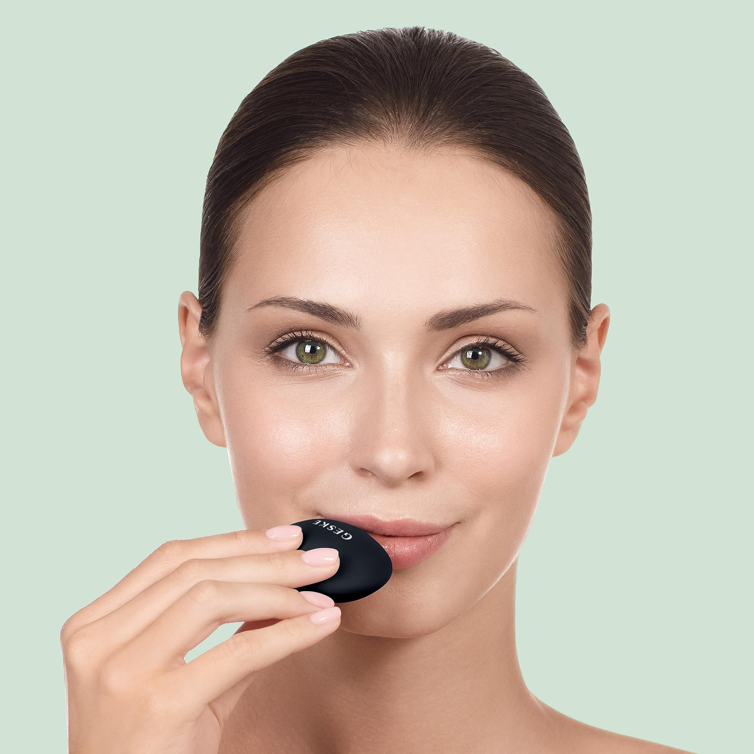 Mujer sujetando masajeador facial negro. Primer plano, fondo verde.