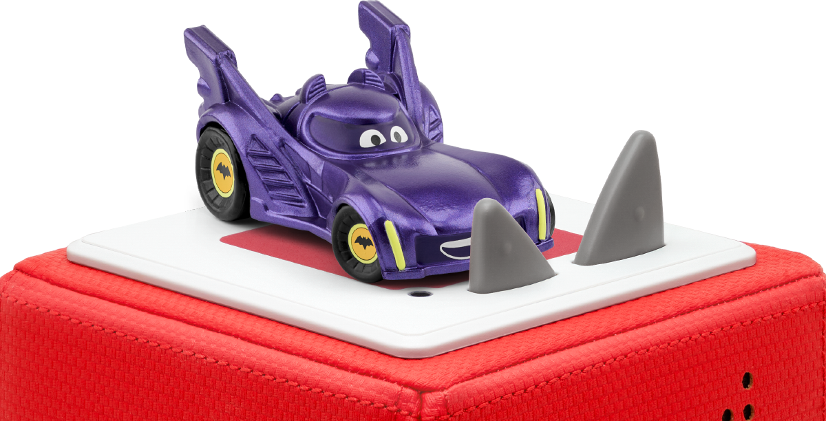 Ein lila Spielzeug-Batmobil steht auf einer weißen Plattform mit Haifischflossen. Es steht auf einem roten Sockel.