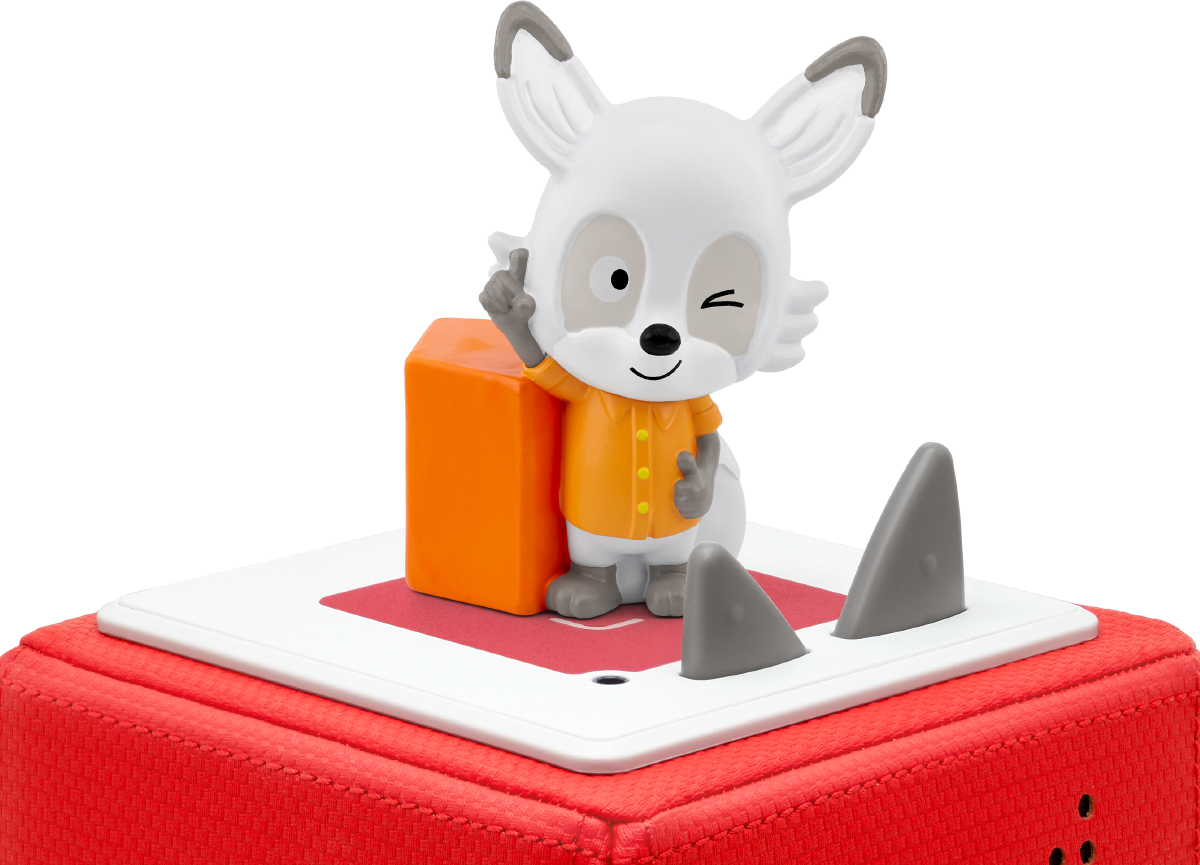 Ein weißes Fuchspielzeug mit orangefarbenem Hemd und zwinkerndem Auge steht auf einem roten Würfel mit grauen Flossen. Links ist ein orangefarbener Block.
