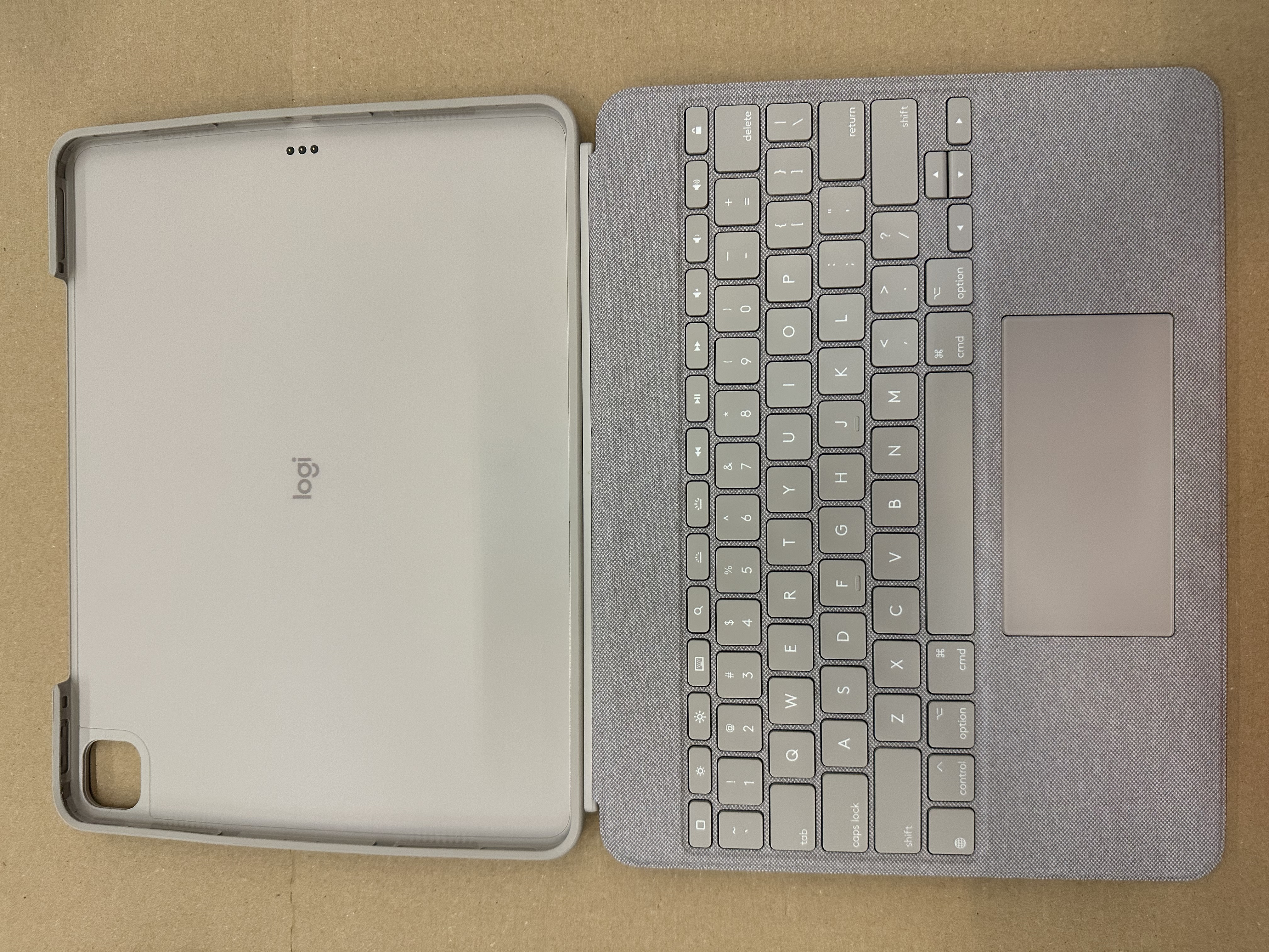 Jasnoszara tablet z klawiaturą i gładzikiem, otwarty na brązowej powierzchni.