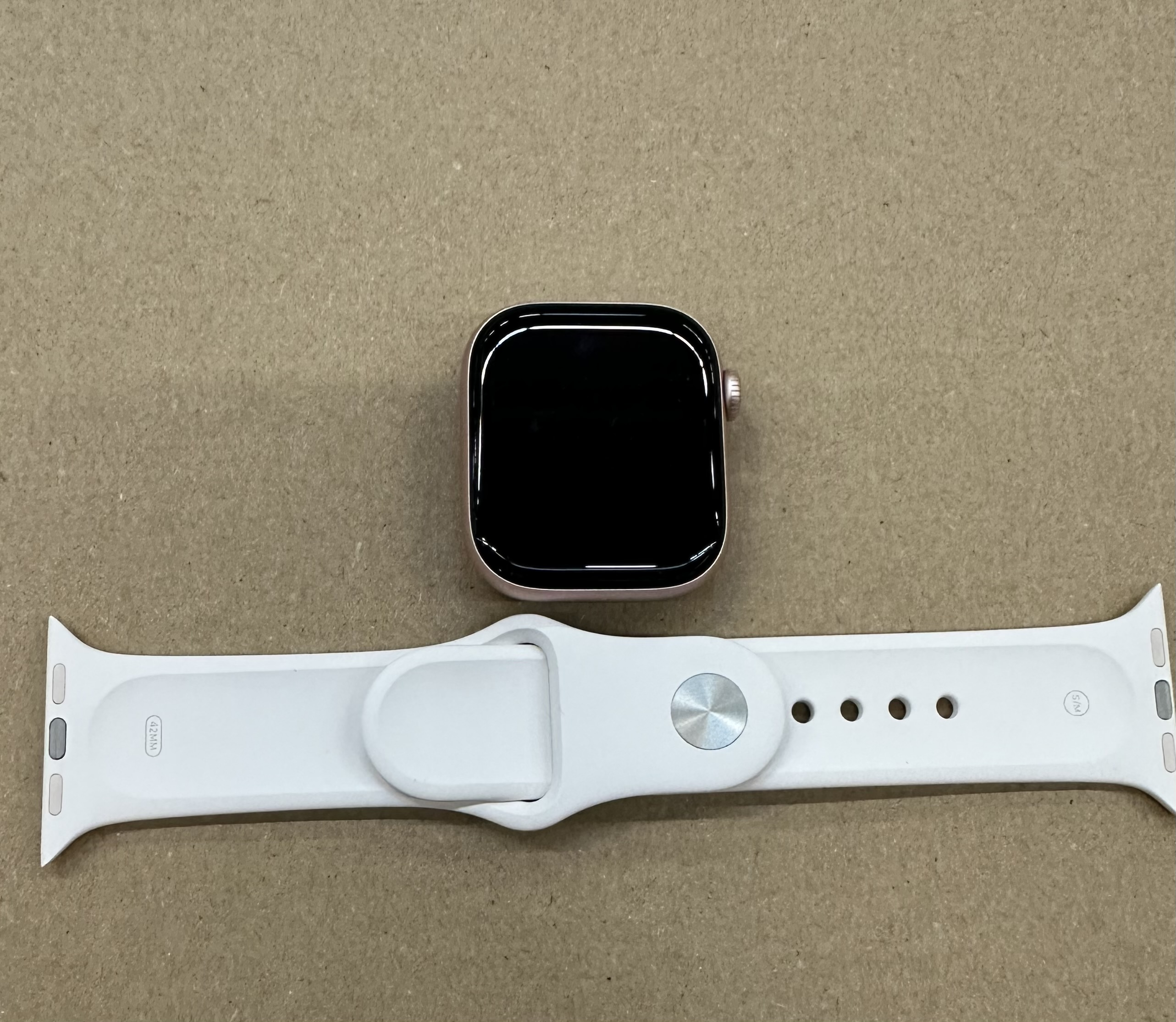 Złoty Apple Watch z białym paskiem leży na brązowej powierzchni.