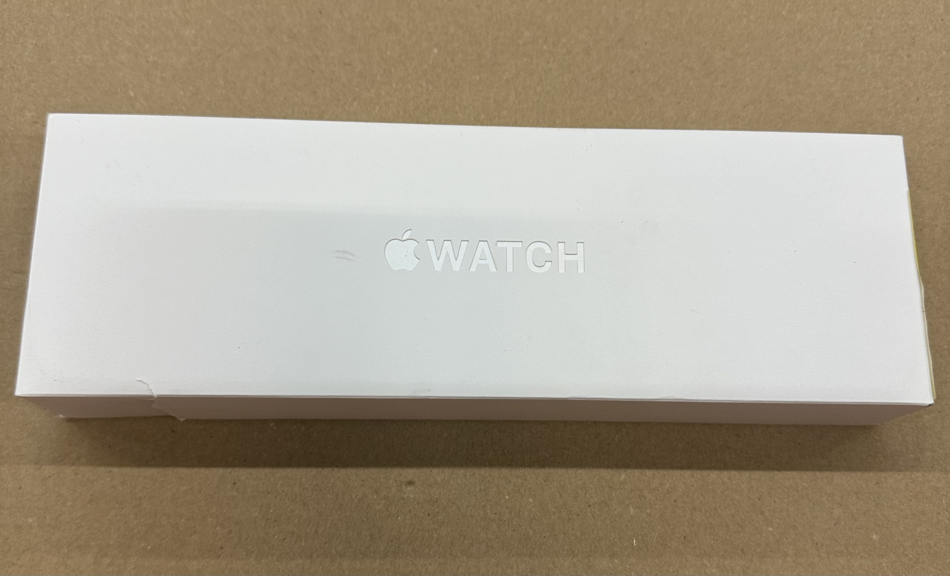 Białe pudełko Apple Watch na brązowym tle.