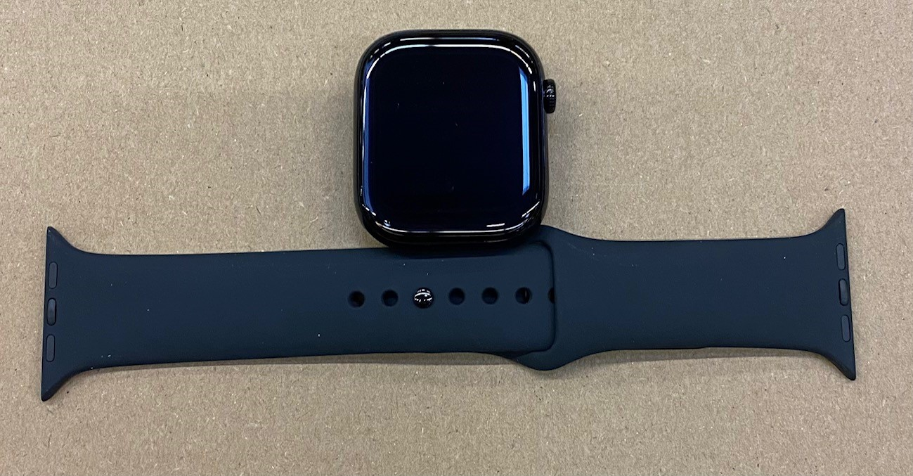 Czarny smartwatch z czarną opaską na brązowym tle.