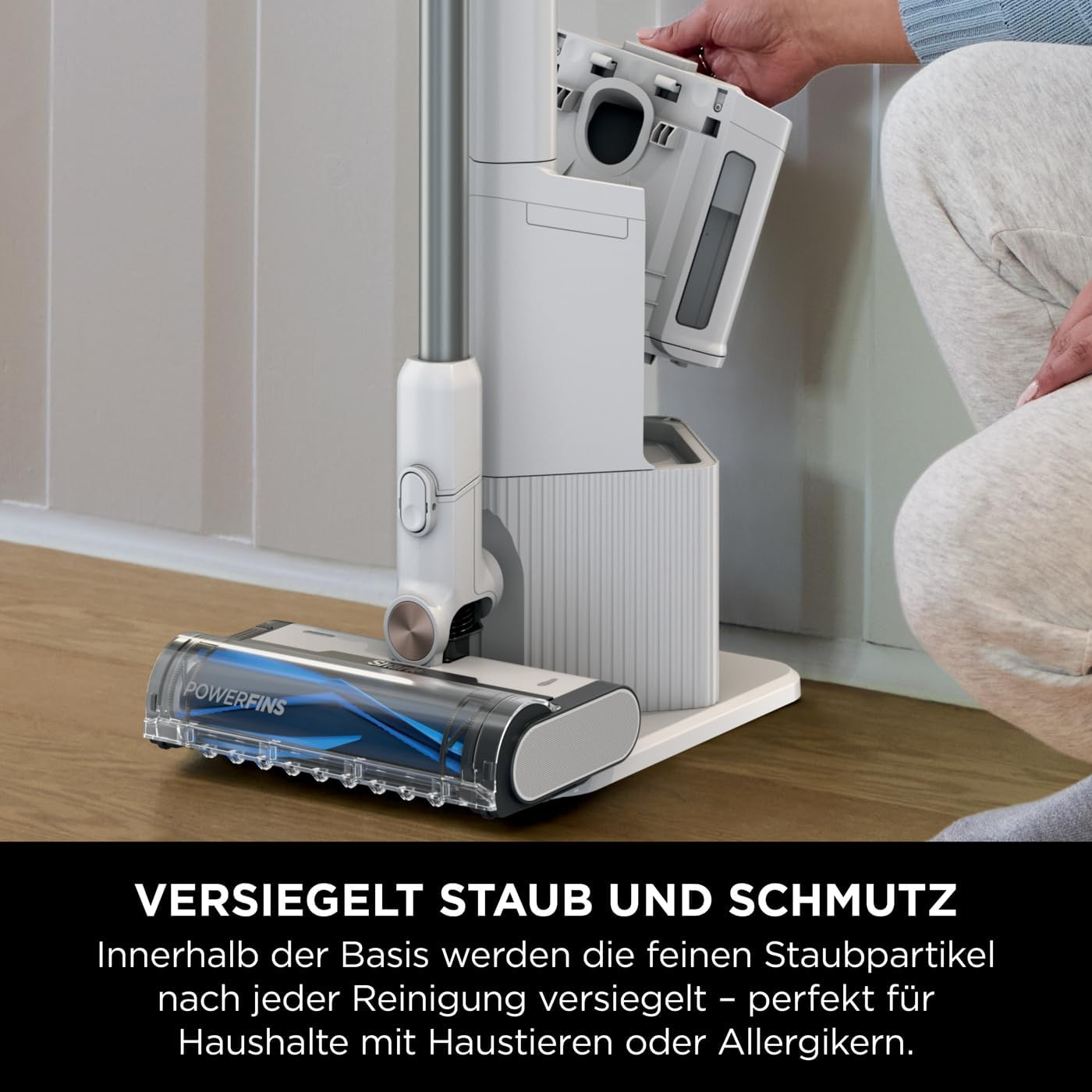 Ein weißer Staubsauger und seine Ladestation. Eine Person hält den Staubbehälter.