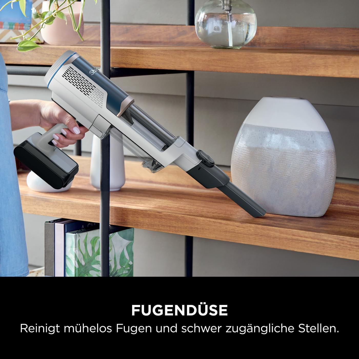 Person hält einen Handstaubsauger, in der Nähe eines Regals mit Dekor.