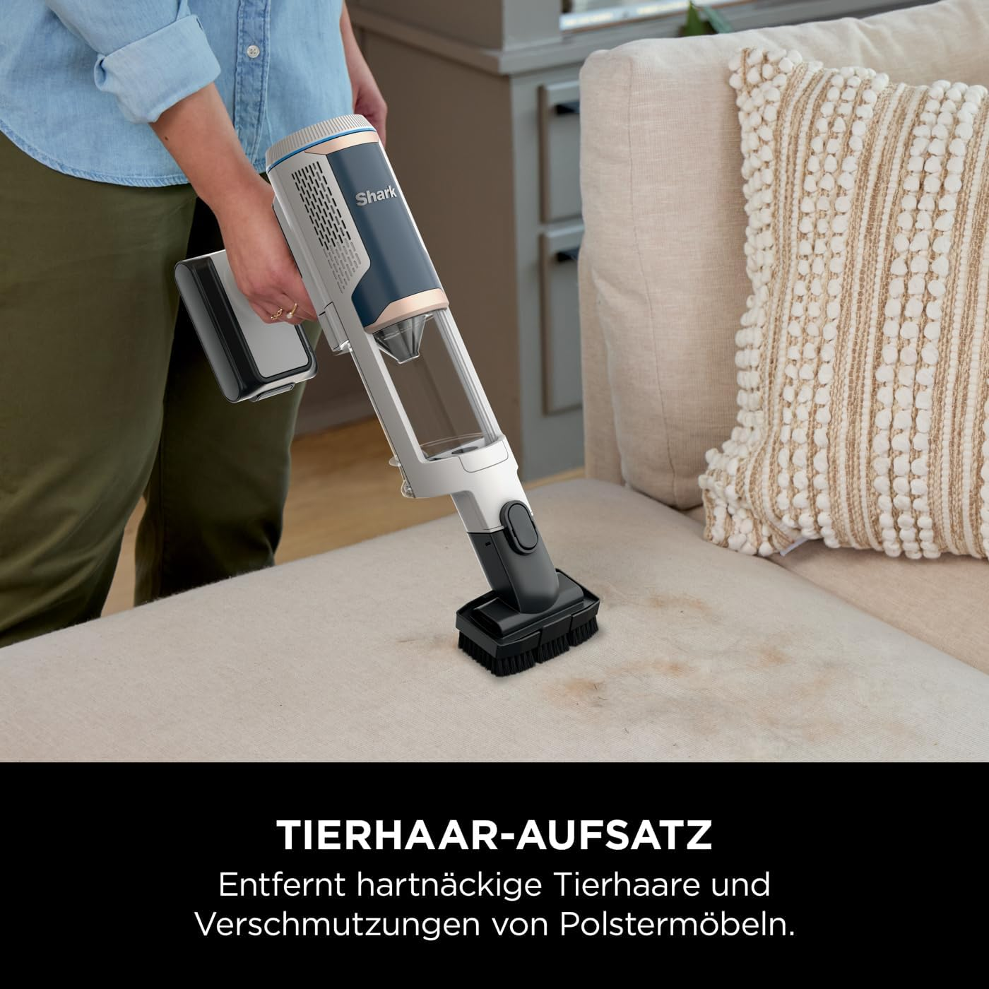 Eine Person saugt ein beiges Sofa ab und entfernt Schmutz mit einem Handstaubsauger.