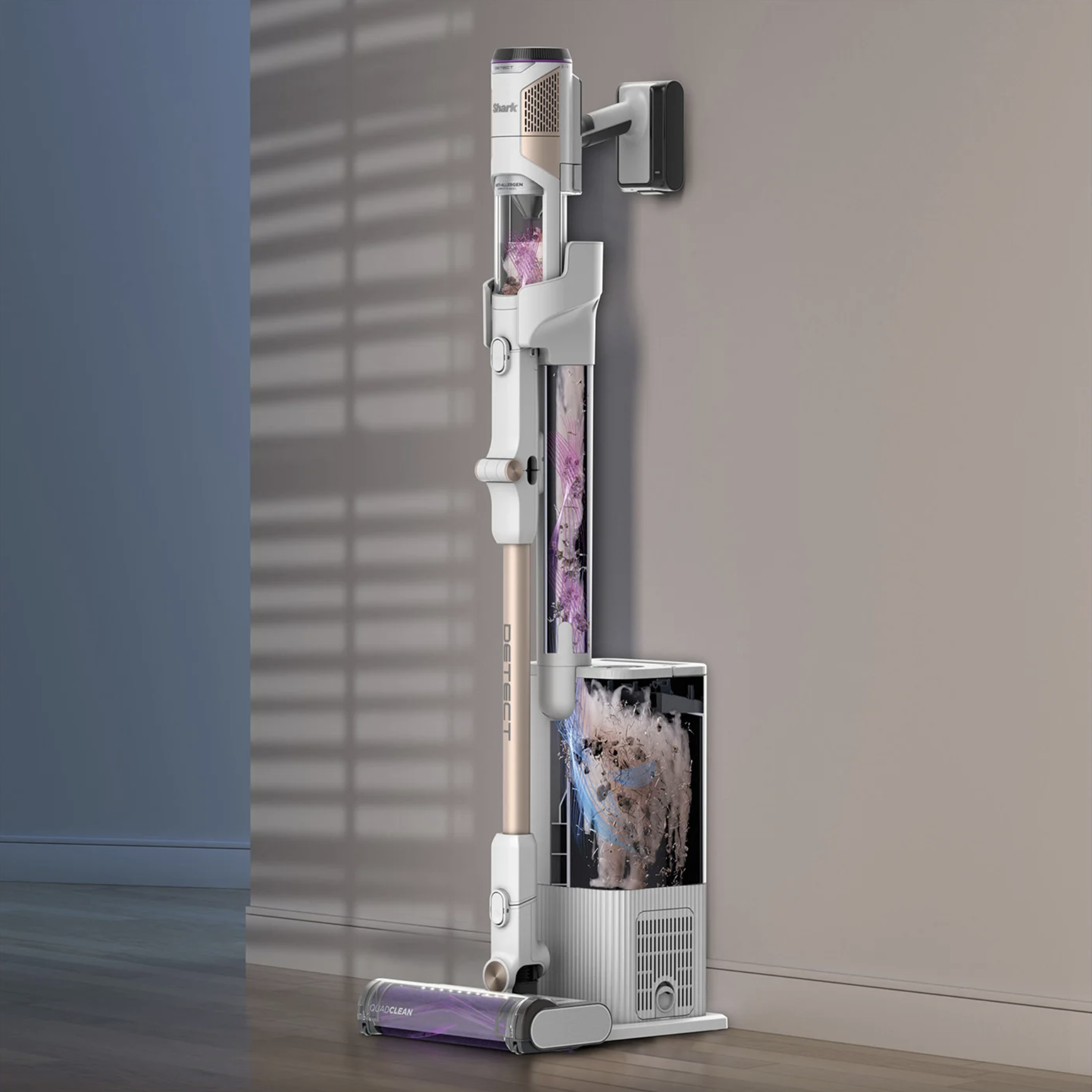 Aspirateur blanc et doré posé sur une base de chargement. Un support mural est également visible.