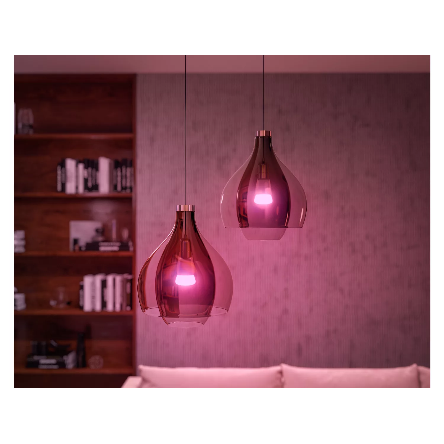 Two pendant lights with pink light, hanging in a room with a wooden bookshelf.