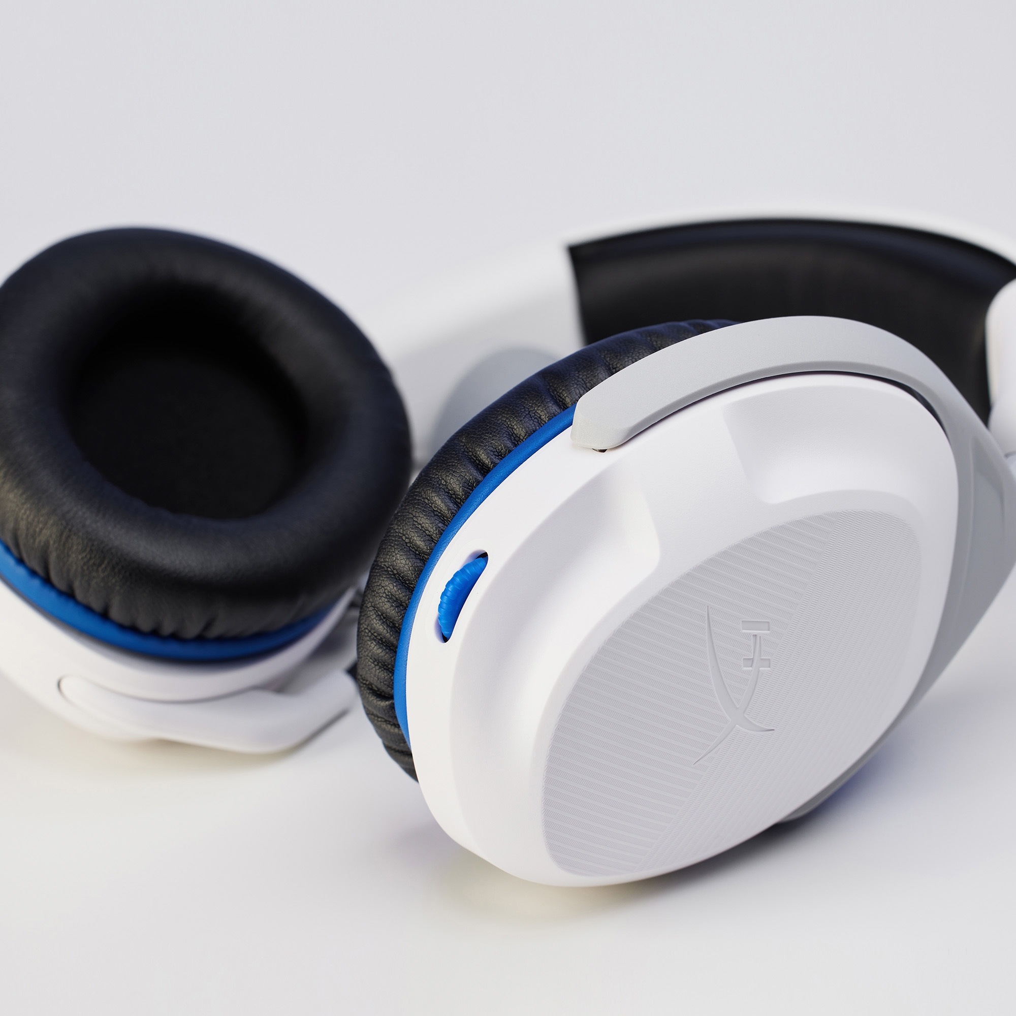 Weiße und graue HyperX-Kopfhörer auf weißer Oberfläche. Blaue Akzente sind sichtbar.