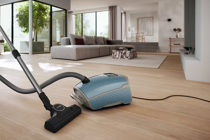 Ein blauer Staubsauger auf einem Holzboden, mit Staubsaugerschlauch und modernem Wohnzimmer.