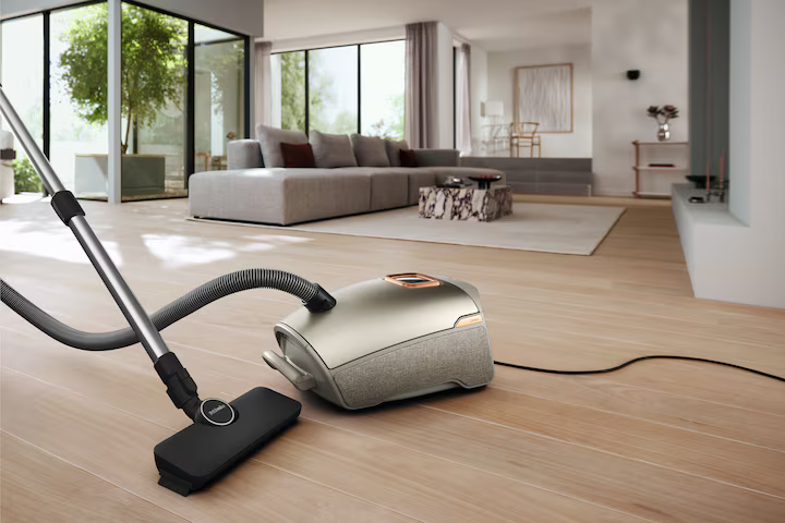 Ein Staubsauger in Beige und Grau mit Düse, auf Holzboden in einem Wohnzimmer.