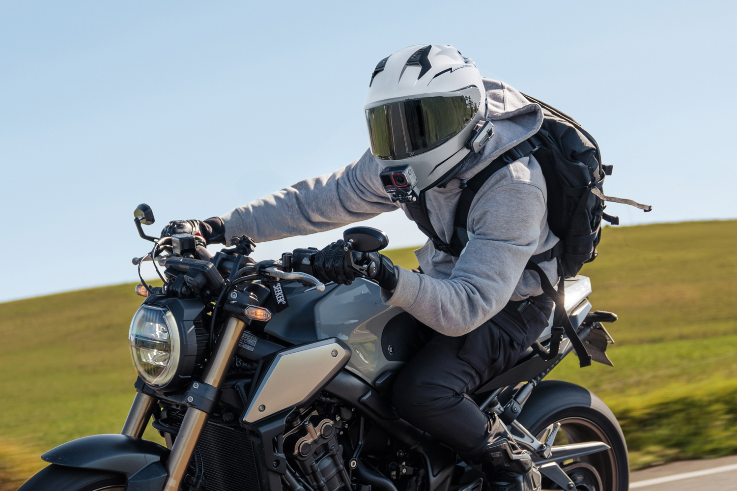 Una persona montando en moto en una carretera. Llevan casco, mochila y ropa gris.
