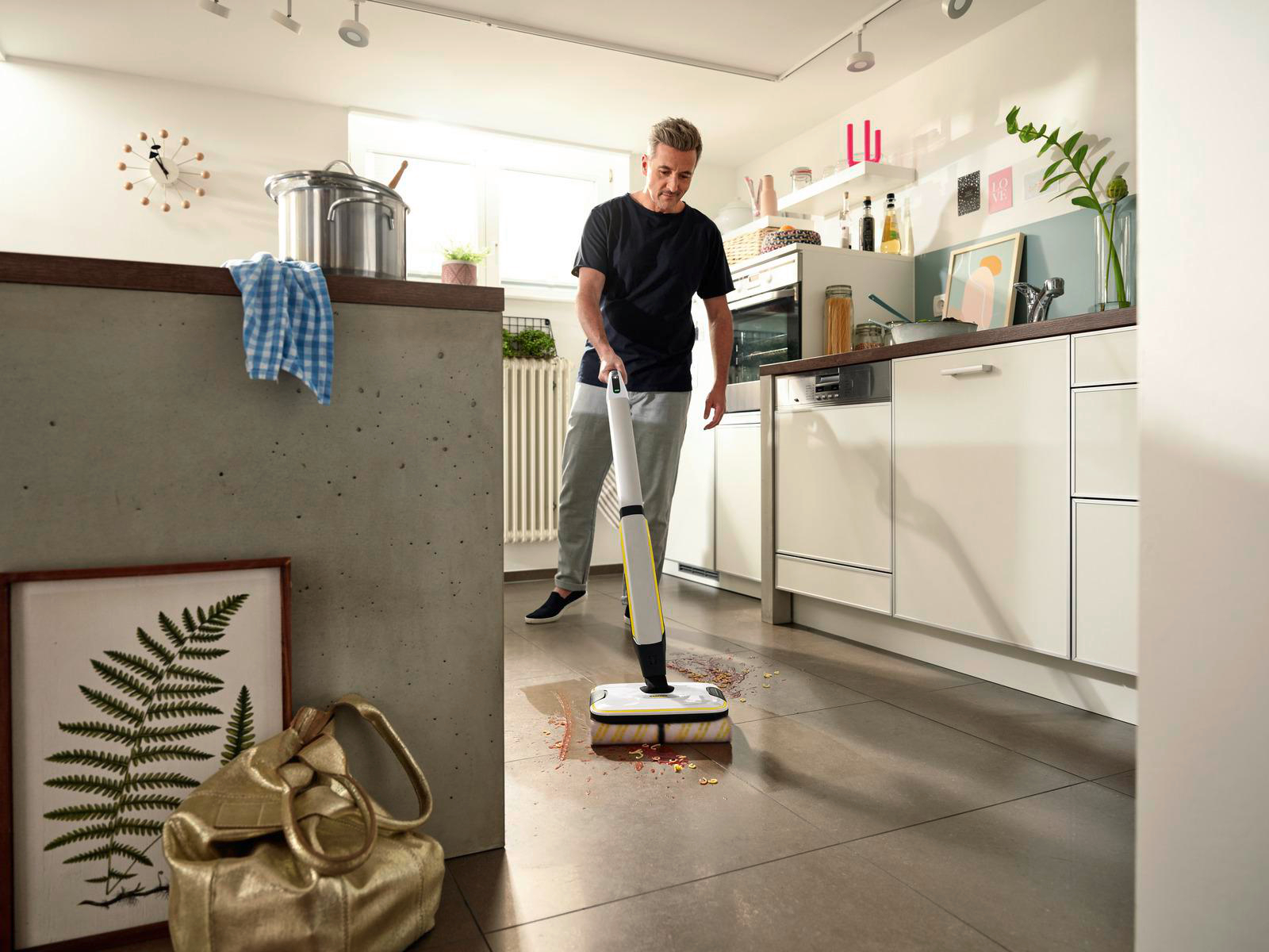 Ein Mann reinigt einen Küchenboden mit einer Reinigungsmaschine. Die Küche hat weiße Schränke und Geräte.