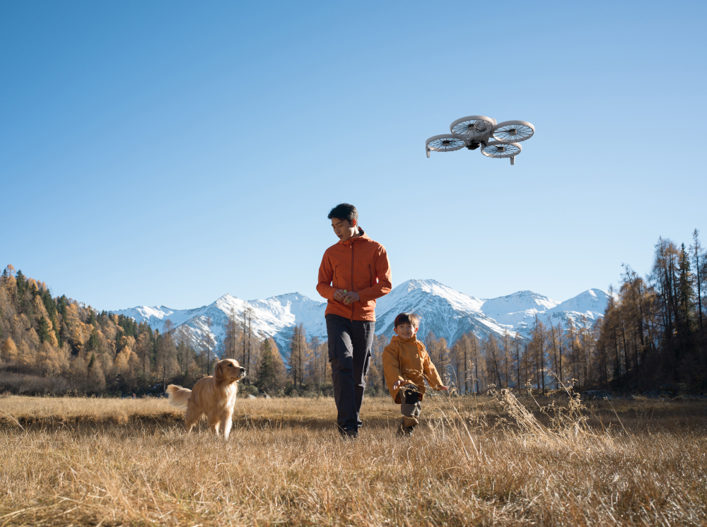 Mężczyzna i dziecko idą z psem, dron leci, góry w tle.
