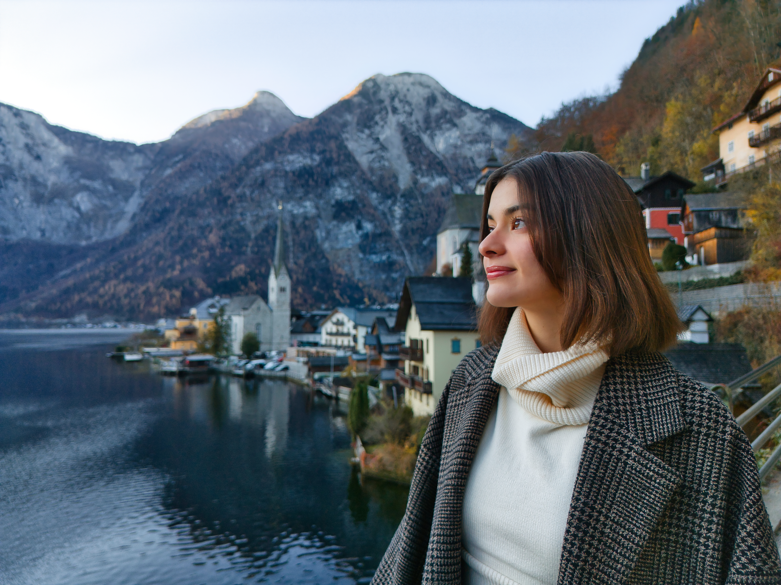 Donna guarda lago e montagne, cappotto, in un ambiente cittadino.