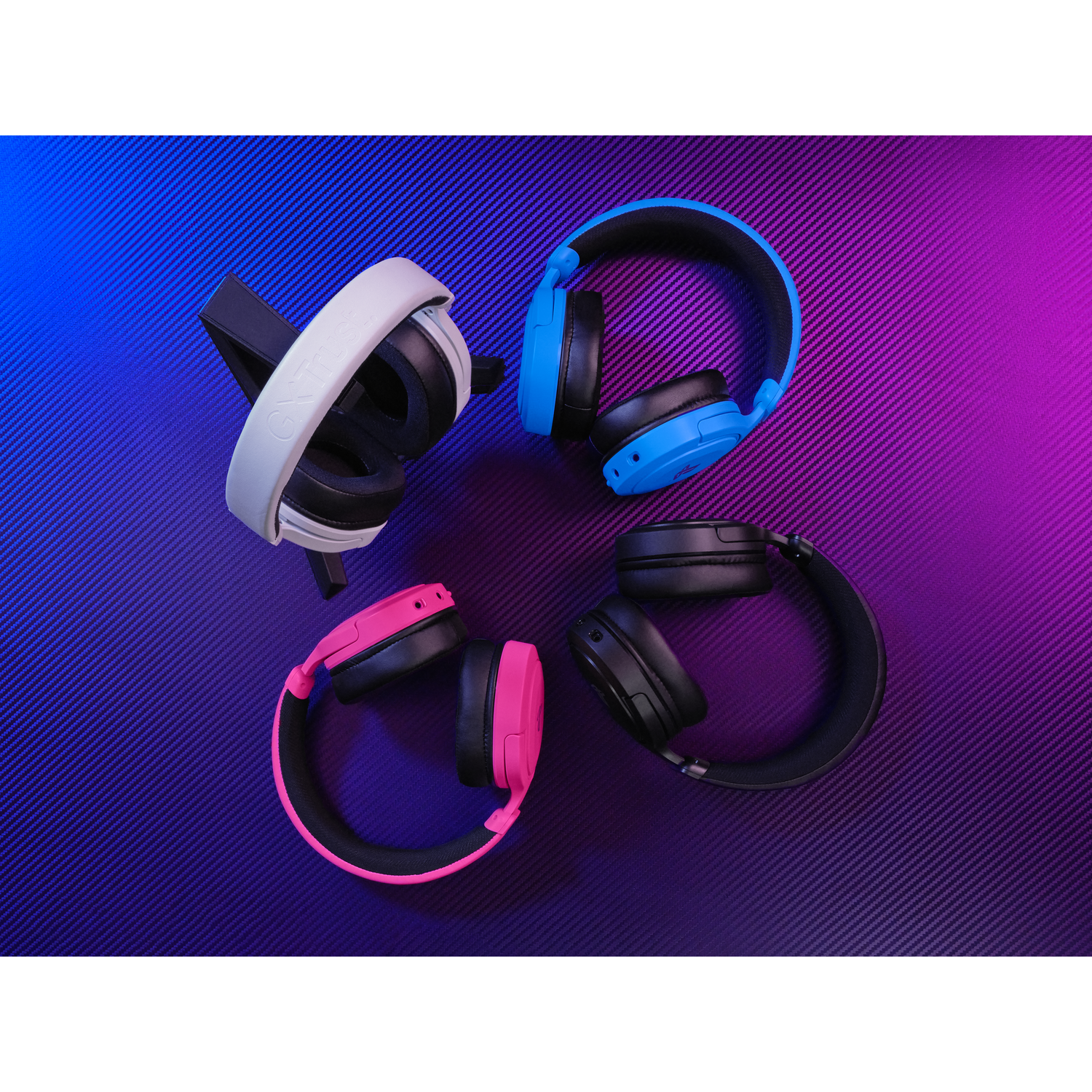 Four gaming headsets: white, blue, pink, and black, on a purple-blue background.