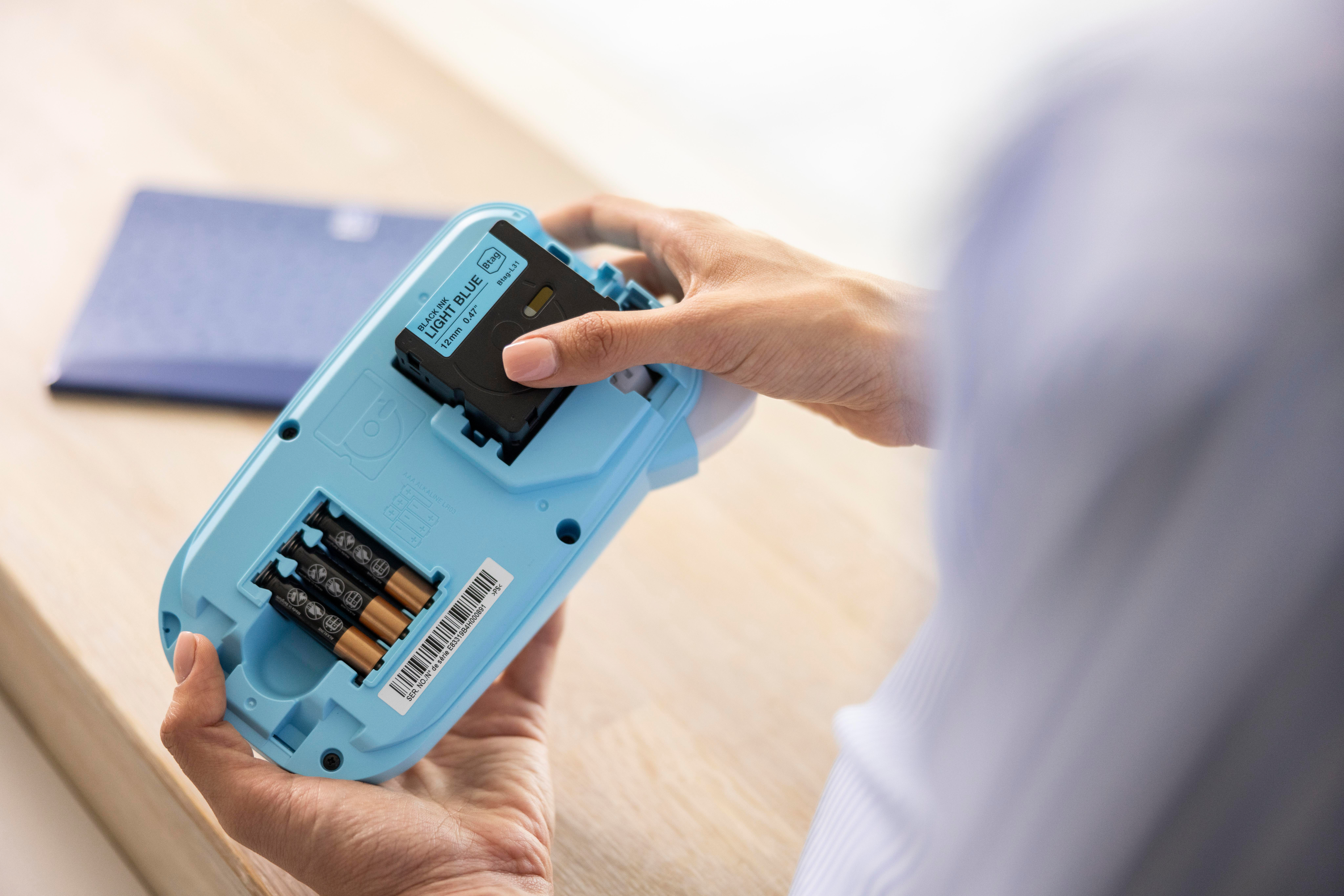 Person öffnet die Rückseite eines blauen Etikettendruckers zum Batteriewechsel.