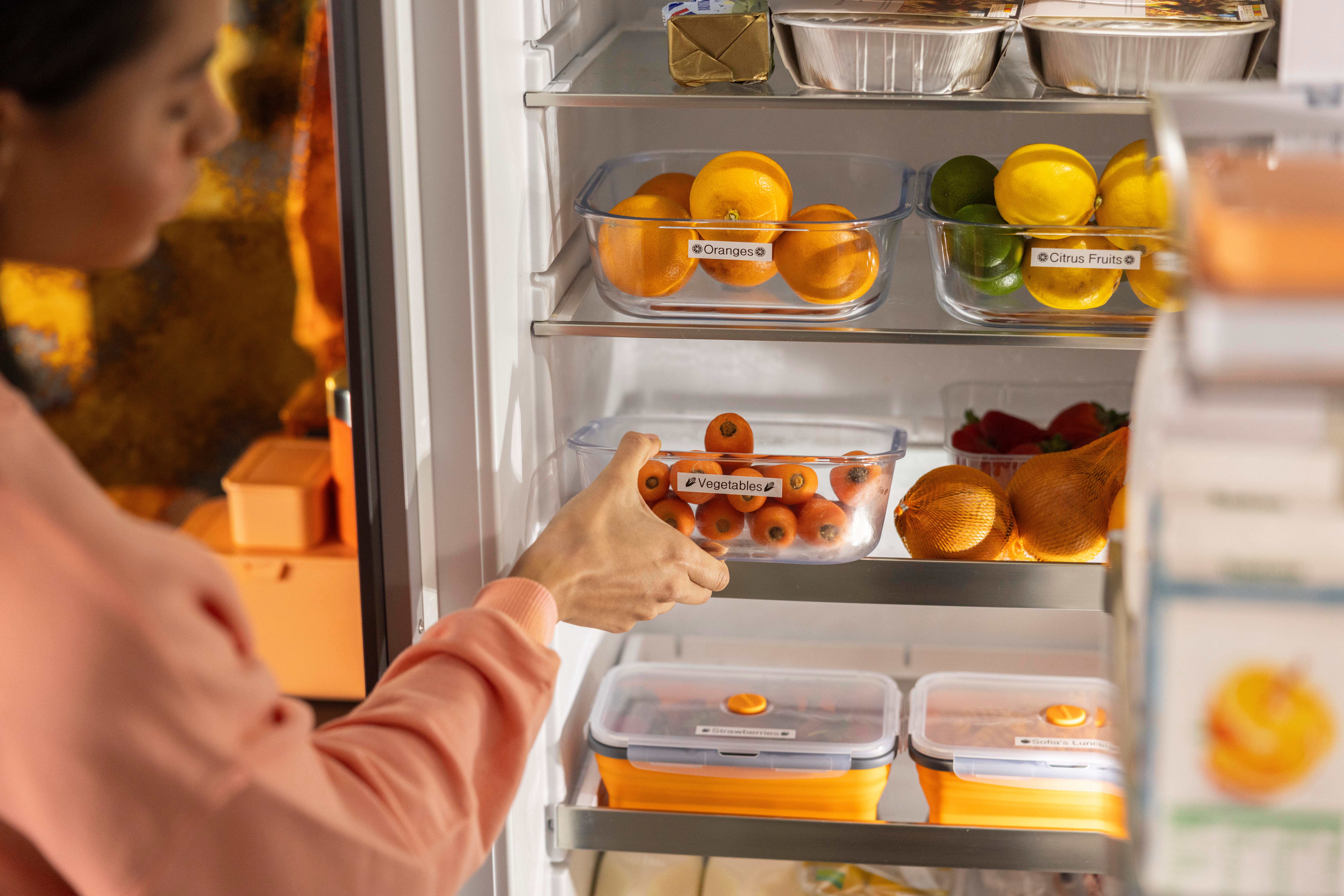 Die Hand einer Person, die in einen Kühlschrank mit Obst greift.