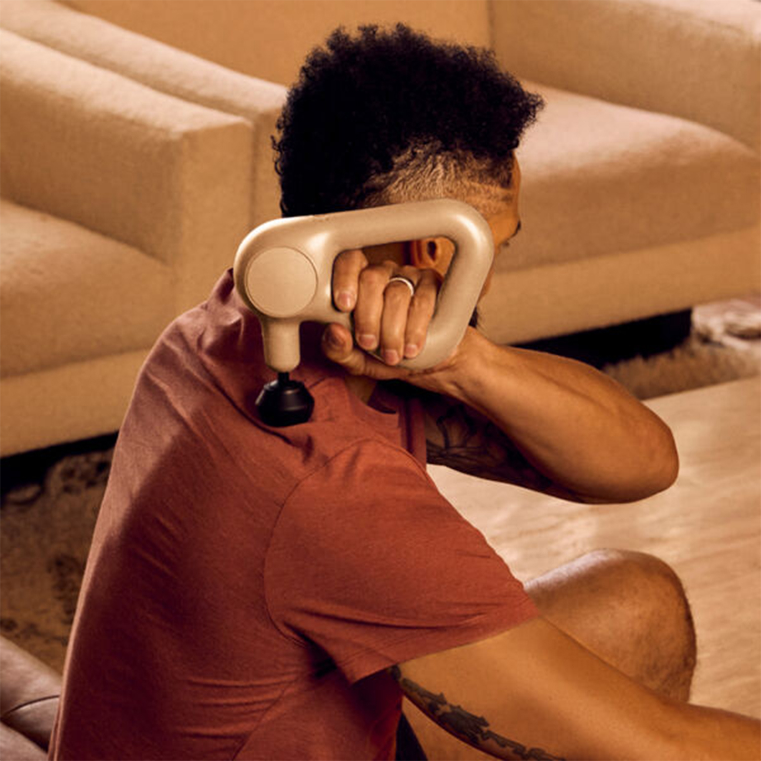 Un uomo si massaggia la spalla con uno strumento per massaggio portatile beige.